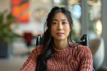 Close-up of an Asian professional seated in a wheelchair, working in a bright, accessible office. The employee is part of a diverse team, reflecting the company focus on DEI. The modern workspace