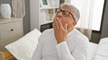 Fototapeta premium Middle-aged man yawning in a bright modern bedroom, portraying a relaxed morning at home