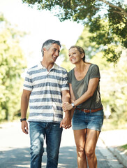 Obraz premium Laugh, holding hands and happy couple in road walking for bonding, relationship and love outdoors. Nature, marriage and mature man and woman for romance, affection and relax on weekend together