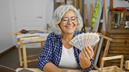 Smiling mature woman holding polish zloty in a carpentry workshop