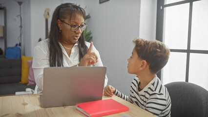 A woman guides a boy during homework on a laptop in an indoor living room setting.