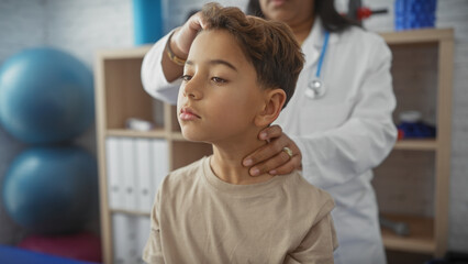 A female doctor examines a young boy in a medical clinic, suggesting a routine check-up or physiotherapy session.