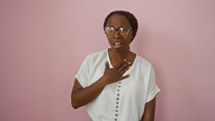 Woman expressing surprised emotion with hand on chest, standing against isolated pink background, wearing glasses and white shirt