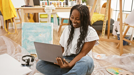 A smiling african woman with curly hair using a laptop in a creative indoor studio