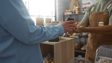 Baker handing coffee to customer at bakery counter indoors with pastries in the background.