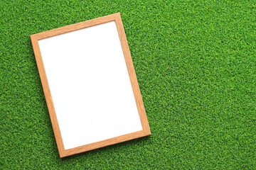 Empty frame for photo or text with a white sheet on a background of green grass. Artificial green grass leaf and simple wooden frame. Place for text