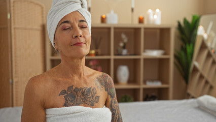 Woman enjoying relaxation in a spa room with candles and plants, wrapped in a towel and a turban
