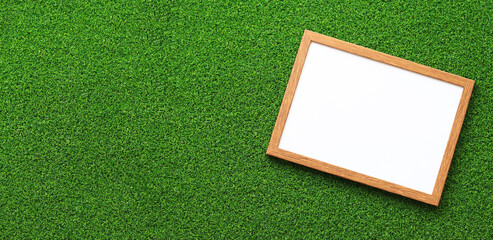 Empty frame for photo or text with a white sheet on a background of green grass. Artificial green grass leaf and simple wooden frame. Place for text