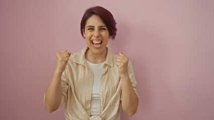 A jubilant young woman with short hair celebrates enthusiastically against an isolated pink...
