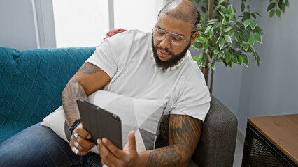 Handsome bearded african american man using tablet indoors on a couch at home