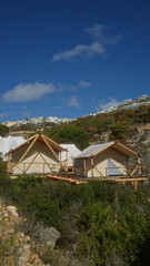 Camping tents nestled in an african nature setting under a clear blue sky with nearby hills and vegetation, showcasing an adventurous outdoor experience.
