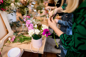Woman florist in green jacket forms a fresh bouquet of white, and pink flowers in a box