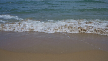 Sandy beach with gentle waves lapping the shore on a clear and tranquil day, showcasing a beautiful outdoor coastal scene.