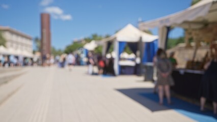 Blurred outdoor scene in mallorca with people enjoying a sunny day at a market featuring tents and defocused shops in the background.