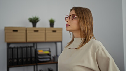 Attractive blonde woman in an office room looking to the side with shelves and plants in the background.