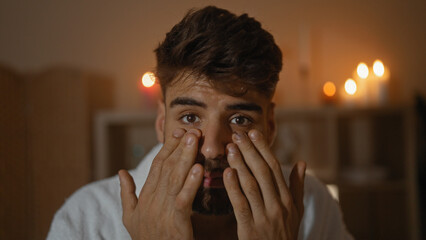 Young man with a beard in a spa wellness center, illuminated by candlelight, gently massaging his...