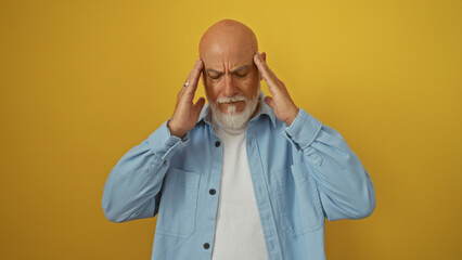 Obraz premium Man grey-haired bald mature holding head in frustration against yellow background wearing light blue shirt