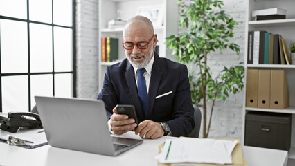 A senior man in a suit smiles at his phone in a modern office.