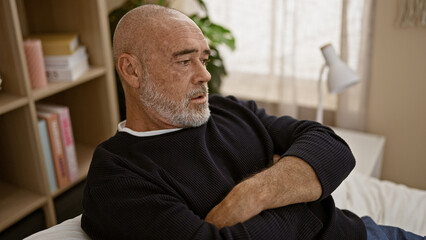 Mature bearded man sitting thoughtfully in a cozy room at home, exuding a contemplative mood.