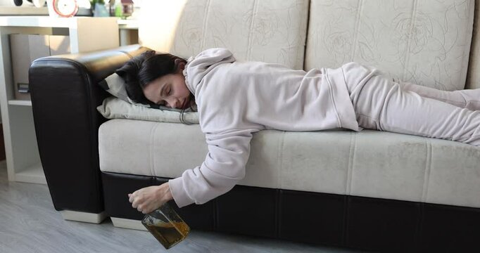 Drunk young woman sleeping on couch with bottle. Alcoholic depression and divorce concept