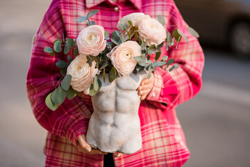 Vase in the form of a male torso with a bouquet of big peonies in hands of a woman