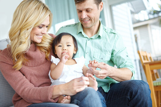 Adoption, happy family and parents with baby in home for love, support or bonding together. Mother, father and cute foster kid with people for interracial connection, care and playing with orphan