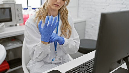 A focused young caucasian woman in a laboratory wearing a lab coat and blue gloves working with a...