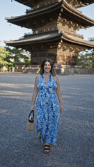 Confident and carefree, a beautiful smiling hispanic woman casually walks towards the camera, posing infront of the majestic to-ji temple in kyoto, japan.