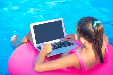 Young girl in inflatable circle in swimming pool using her laptop computer.