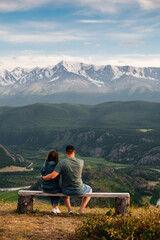 a couple in love sits on a bench and looks at the snow-covered peaks