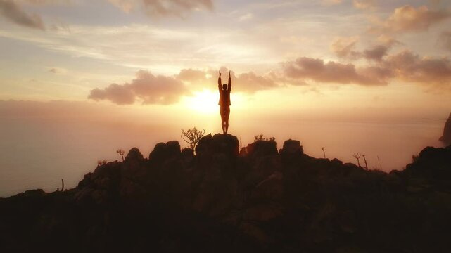 Person standing on a rocky cliff at sunset and exercising with the ocean in the background