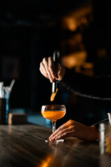 Bartender adds orange peel to cocktail using special tongs.