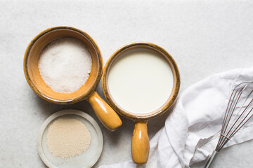mise en place of ingredients for making bread, overhead view of ingredients for proofing yeast, yeast milk and sugar on a white marble countertop