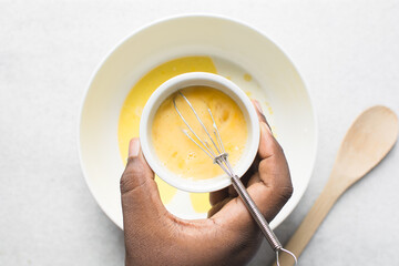 Overhead view of whisked raw egg in a ceramic ramekin, whole raw egg in a white ramekin
