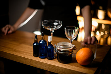 Various cocktail glasses, jars with pipettes and sprays and an orange standing on the bar table