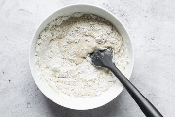 Overhead view of nigerian puff-puff dough being mixed with a wooden spoon, puff-puff dough in a white mixing bowl, process of making puff-puff or bofrot