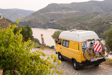 Blonde woman enjoying the view standing by her retro camper van parked in Douro valley. Summer time in Portugal