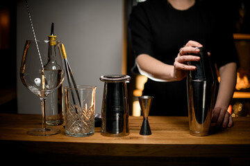 The female hands of the bartender take a shaker, other tools are standing nearby