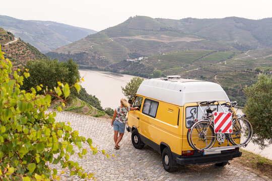 Blonde woman enjoying the view standing by her retro camper van parked in Douro valley. Summer time in Portugal