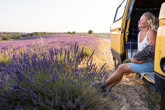Young blonde woman enjoying the view in her retro yellow camper van at sunrise in Valensole lavender fields in Provence, France