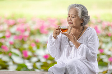 Elderly Woman Enjoying a Cup of Tea in a Lush Garden with Pink Water Lilies, Embracing Tranquility and Relaxation in Nature While Wearing a White Outfit