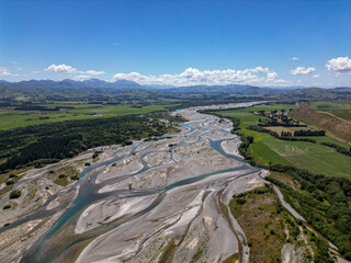 Aerial view of braided river formed from glacial melt and sediment. Shallow channels of water interweave into the mountains on the horizon