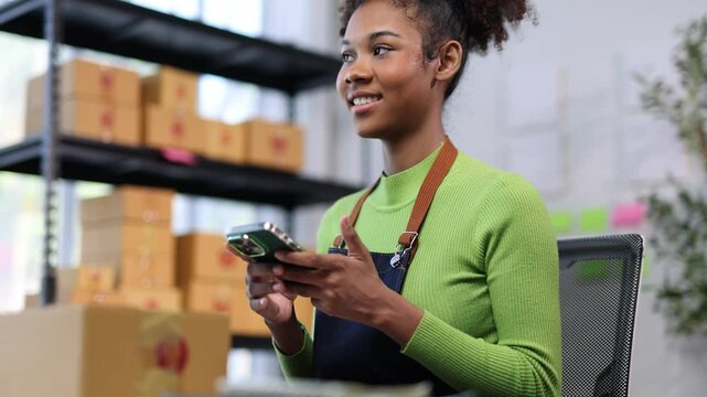 Small business owner checks her smartphone while efficiently packing products in an organized workspace, showcasing a modern and effective business operation.