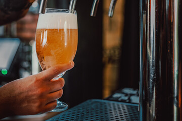 Close-up of a hand holding a glass of beer with a tap in the background, depicting a bar scene
