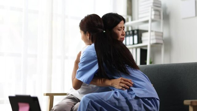 Nurse comforting worried patient with empathy. Nurse providing emotional support to a concerned patient at home, expressing empathy and care by comforting with a hug on a sofa.