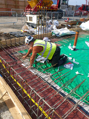 Radon gas membrane inspection at a construction site with workers in safety gear. Slab reinforcement bars and green membrane installation for foundation work. Close-up view.