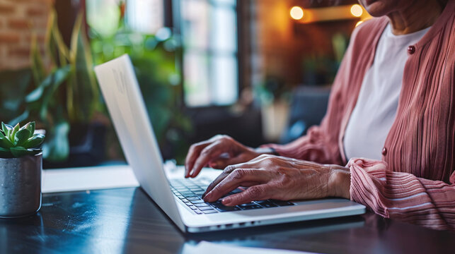 Close-up of a senior woman using a laptop to browse the internet, focusing on her hands on the keyboard and her attentive expression  - Powered by Adobe