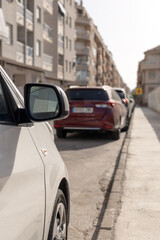 Fototapeta premium Line of parked cars along a narrow city street. Perfect for content related to urban transport, city living, automotive articles, or traffic management strategies. Parking price. Vertical picture.