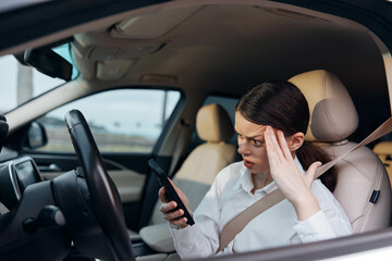 Car driver, stress, cell phone a woman in the driver's seat of a car holds a cell phone in one hand and rests her other hand on her forehead, appearing stressed or worried