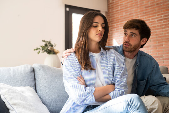 Close-up of a young couple sitting apart discussing having relationship problems, thinking about breakup or divorce. Family lovers, distraught men and women, avoid talking and suffer relationship